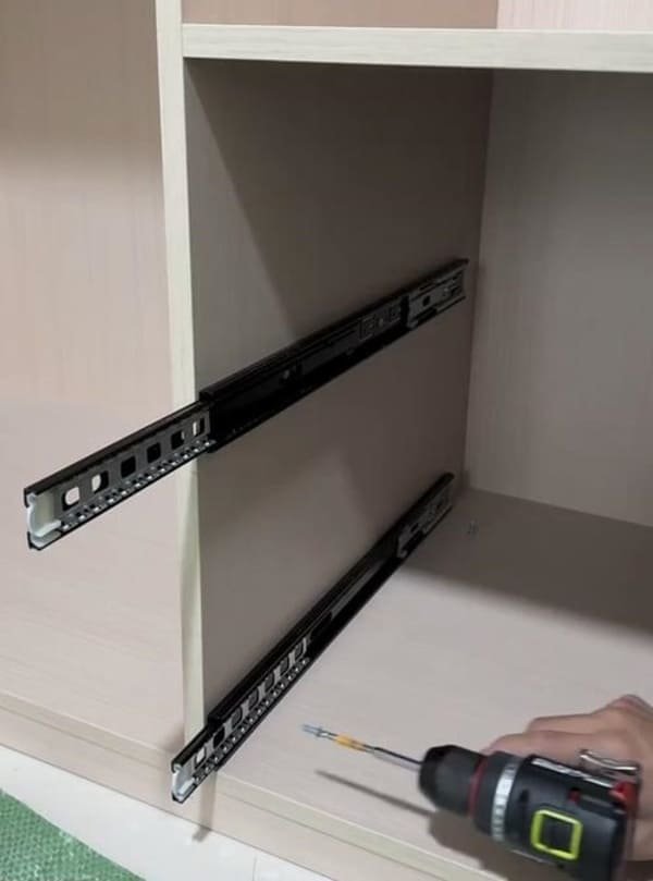 A tradesperson using a level to align a drawer slide inside a cabinet frame.