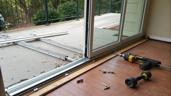 A person carefully lifting a sliding glass door off its track.