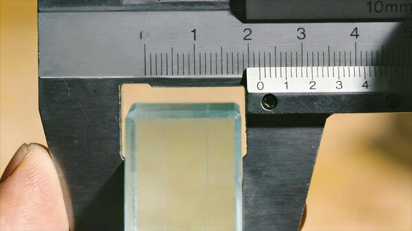 Close-up of a digital caliper showing a measurement on a piece of glass.